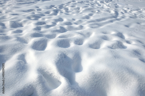 Snow field with many human footprints covered in clear white snow in bright sunny winter day