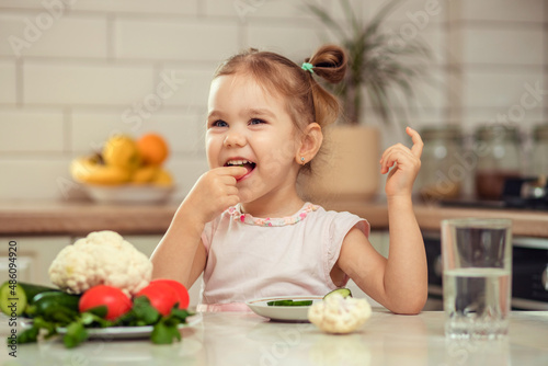 A happy girl 2-3 years old in the kitchen at home or in kindergarten eats delicious and healthy vegetables for lunch.