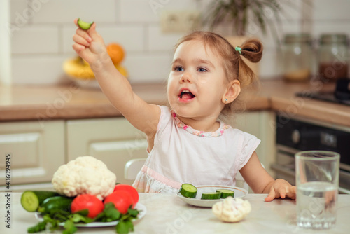 A happy girl 2-3 years old in the kitchen at home or in kindergarten eats delicious and healthy vegetables for lunch.