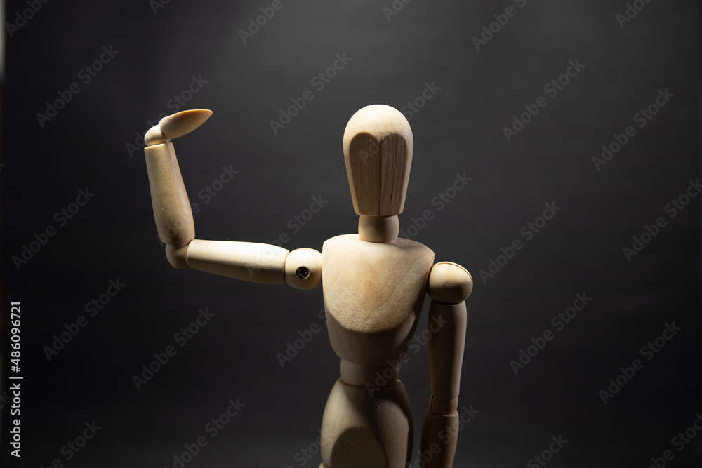 The wooden mannequin raising arm and greets. on a black background The wooden mannequin raising arm and greets. on a black background
