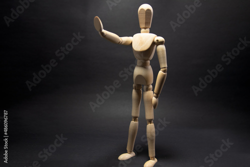 The wooden mannequin raising arm and stop. on a black background