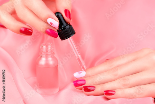 Women s hands with a beautiful manicure in different pink colors. Manicure and cuticle care. A woman s hand drips care oil from a bottle onto her nails.