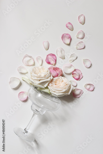 Valentines day or wedding party composition. Cocktail drink glass with pink rose petals and blooming flower heads isolated on white table background. Celebration, love concept. Flat lay, top view.