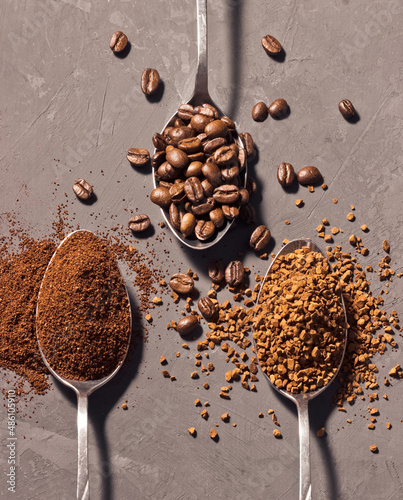 Coffee beans, ground coffee and instant coffee in metal spoons on a dark background.