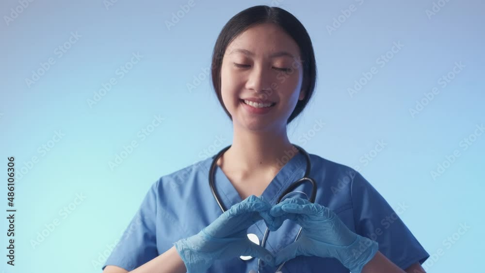 Health care charity. Supportive doctor. Medical volunteer. Portrait of friendly joyful woman nurse showing love heart hand gesture isolated on light blue background. Health care charity. Supportive doctor. Medical volunteer. Portrait of friendly joyful woman nurse showing love heart hand gesture isolated on light blue background.