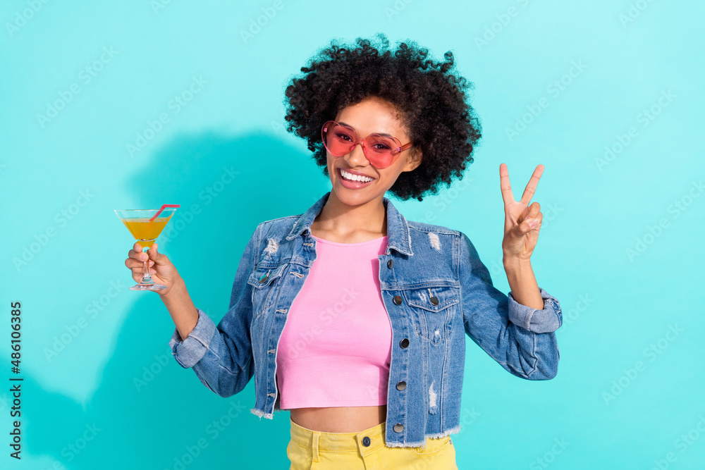 Photo of funny pretty young woman wear jeans jacket eyewear v-sign drinking cocktail isolated turquoise color background