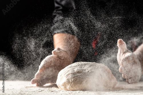 flying pizza dough with flour scattering in a freeze motion of a cloud of flour midair on black. Cook hands kneading dough. copy space