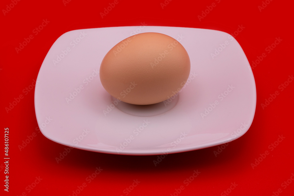 Beige chicken egg on a white saucer on a red background Beige chicken egg on a white saucer on a red background