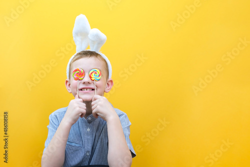 A boy with glasses put on the ears of an Easter bunny hid his eyes behind lollipops.
