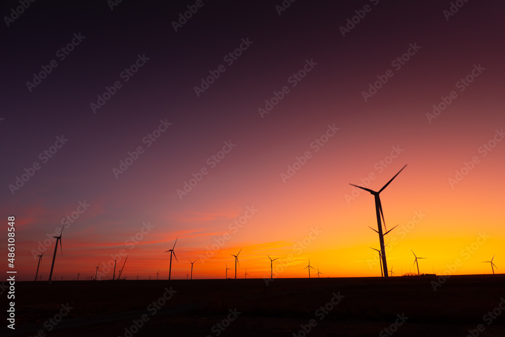 Obraz premium Sunset over an eolian wind farm with amazing sky color. Alternative eco energy good for the environment. Renewable energy industry.