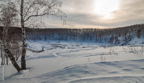 Winter landscape with birch trees on the mountain shore, snow and river