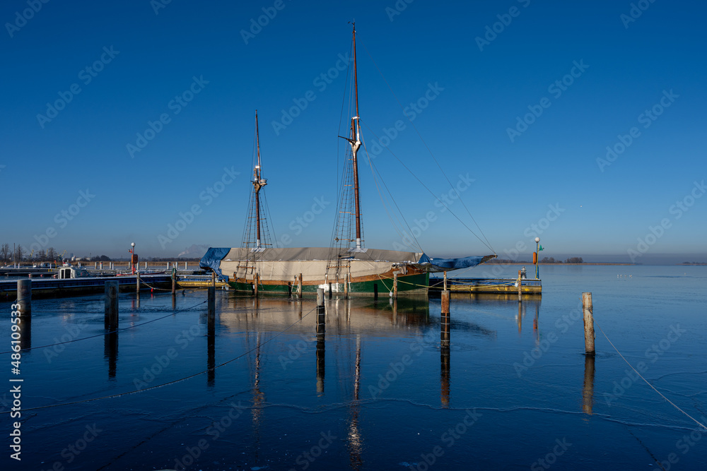 A sailboat in a marina closed down for winter. Blue water and a clear blue sky
