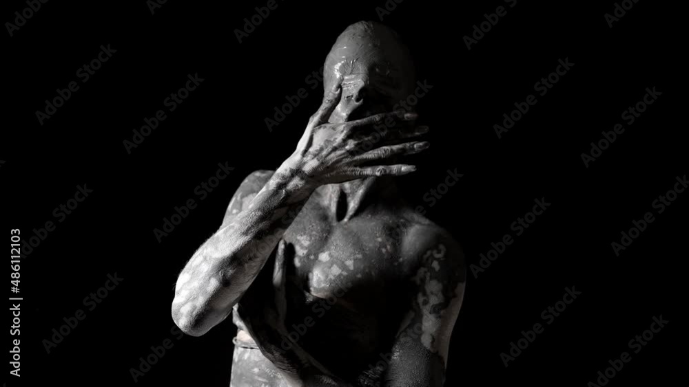 mysterious naked woman with blindfold and skin covered by clay is moving slowly in darkness