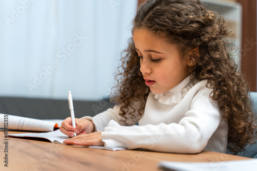 Smart curly girl is thinking about new home task while sitting at online lesson in front of a laptop