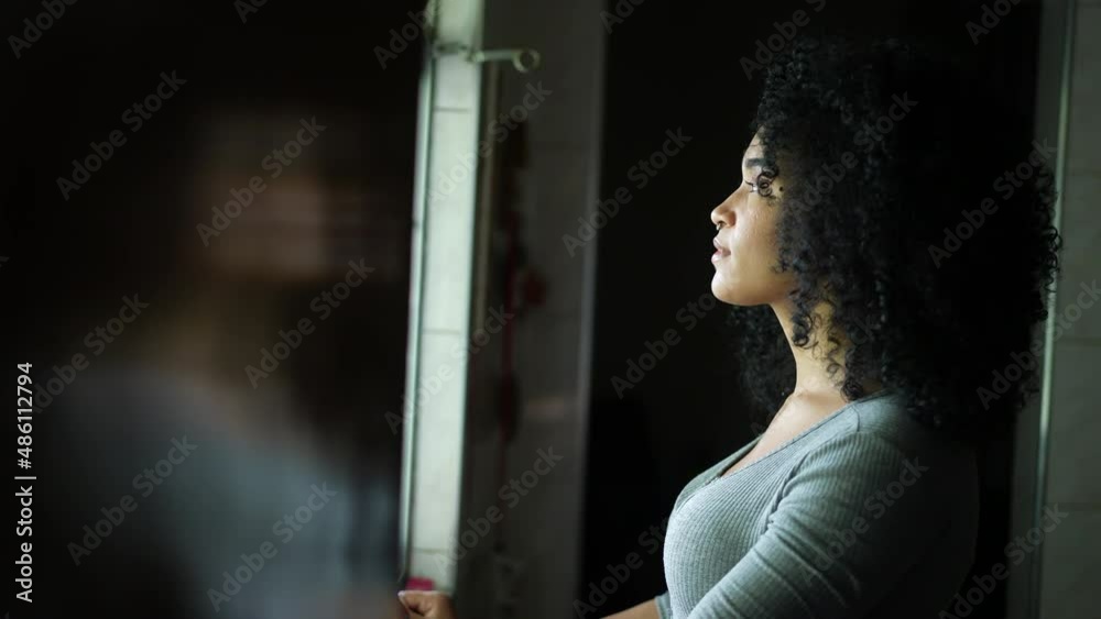A contemplative young woman standing by window looking outside