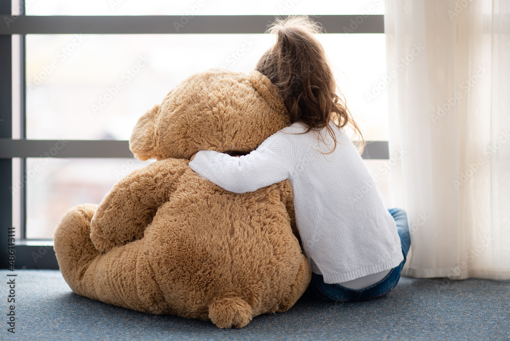 A little girl plays with a big teddy bear. She is dressed in a white jumper. Childhood. Lifestile. A little girl plays with a big teddy bear. She is dressed in a white jumper. Childhood. Lifestile.