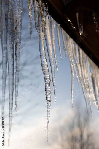 Icy, spring icicles on a wooden house through the setting sun. Selective focus.