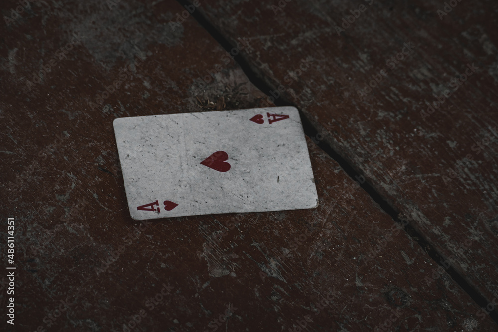 Ace of hearts playing card on dirty wooden surface.
