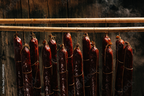 Smoked sausages meat hanging in domestic smokehouse. Clouds of smoke rise up and envelop the sausages hanging in a row. banner, menu, recipe place for text