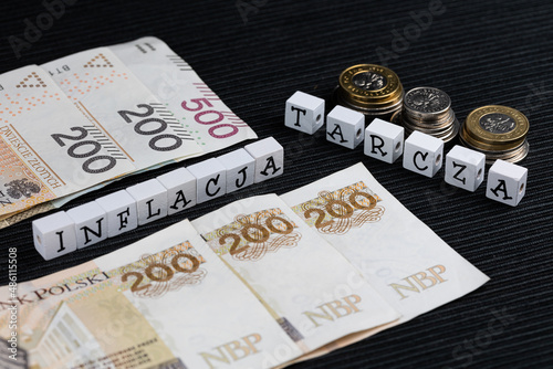 The wording "inflacja" and "tarcza"  translated as "inflation" and "shield" plus Polish coins and banknotes on the black background. High inflation eating savings Polish people.