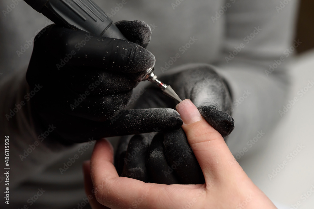 Manicurist makes a hardware manicure to a client of a beauty salon. The device with a cutter-cone removes the old gel-varnish coating and removes pterygium. The concept of beauty and nail care.