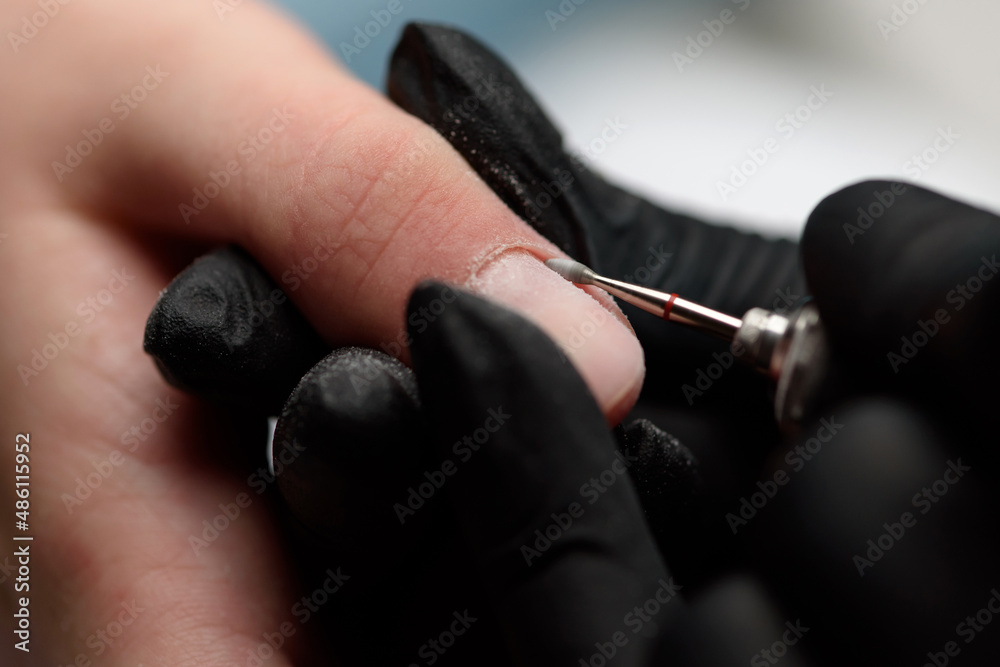 Manicurist makes a hardware manicure to a client of a beauty salon. The process of lifting the cuticle with a cutter close-up. The master uses an electric nail file to trim and remove cuticles.