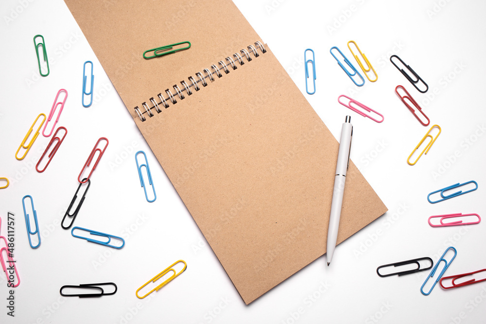 Top view of open spiral blank notebook with pen on white desk background with paper clips. Writing tools. Office supplies. Top view of open spiral blank notebook with pen on white desk background with paper clips. Writing tools. Office supplies.