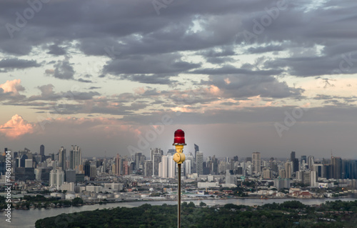 Red lantern of obstruction lights mounted on the rooftop of high rise tall building to ensure flights safety and warn the danger for the plane on the city view background at sunset. Red alarm lamp, No