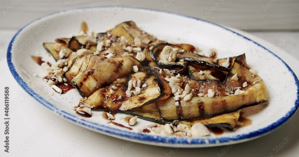Grilled aubergine. delicious vegetables with nuts on a rotating white plate. Grilled restaurant food. Grilled aubergine. Close-up of aubergine roasted. Grilled aubergine. delicious vegetables with nuts on a rotating white plate. Grilled restaurant food. Grilled aubergine. Close-up of aubergine roasted.