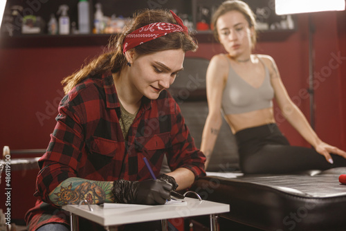 Portrait of concentrated woman in plaid shirt drawing something while sitting in tattoo salon