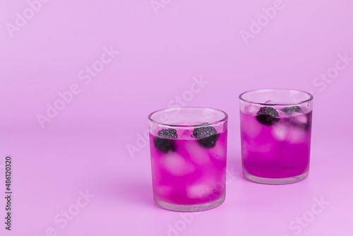 Summer pink cocktail with ice cube and blackberry on pink background.