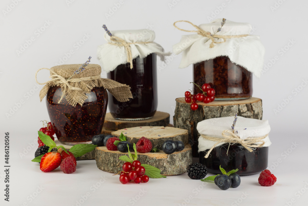 Different seasonal berry jam in jars and empty round natural wooden podium for your products on white background.