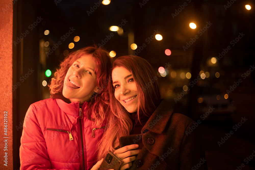 couple of women at night looking at the camera happily illuminated with shop window lights