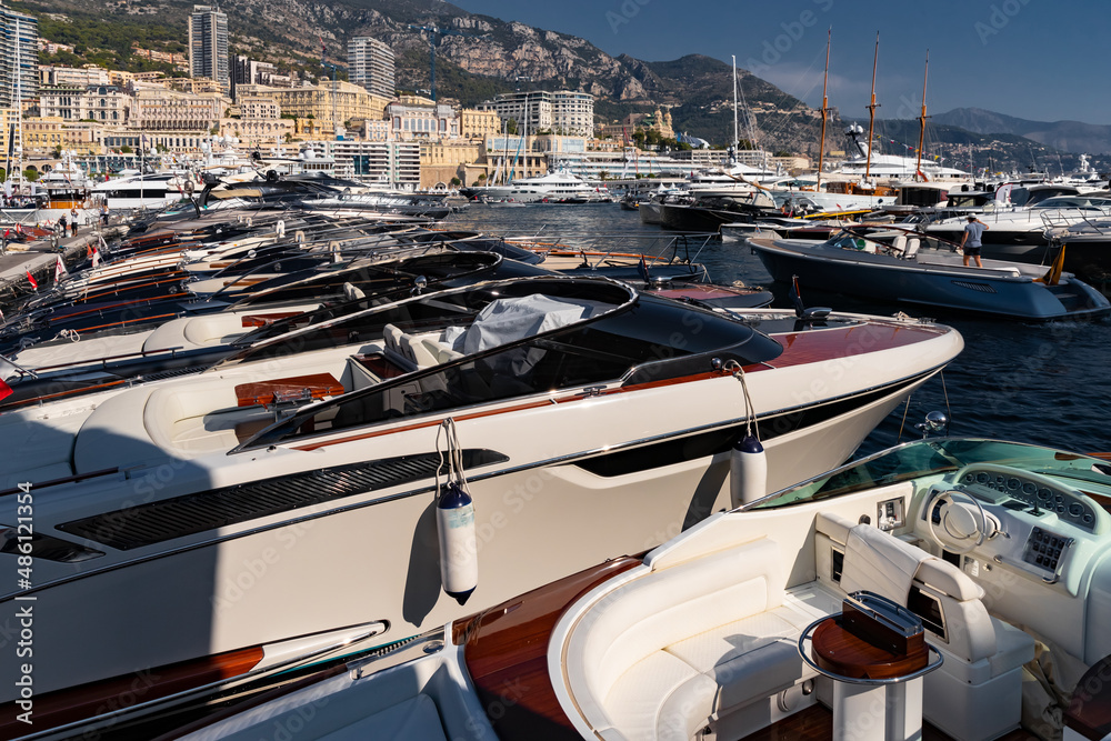 A lot of motor boats in rows are in port of Monaco at sunny day, Monte Carlo, mountain is on background, colourful interior of the boat, are moored in marina, sun reflection on glossy board