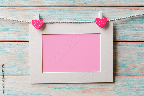 Pink blank card in white frame hanging on a rope over wooden background. Valentines day card with copy space