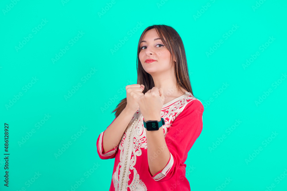 young beautiful moroccan woman wearing traditional caftan dress over green background Ready to fight with fist defense gesture, angry and upset face, afraid of problem. young beautiful moroccan woman wearing traditional caftan dress over green background Ready to fight with fist defense gesture, angry and upset face, afraid of problem.