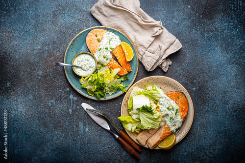 Healthy food meal grilled salmon steaks with dill sauce and salad leafs on two plates on rustic concrete stone background table flat lay from above, diet healthy nutrition dinner, space for text photo