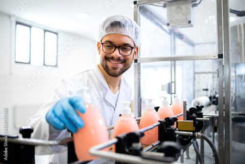 Factory technologist working at production line conveyer machine checking quality of liquid soap or detergent in chemicals industry.