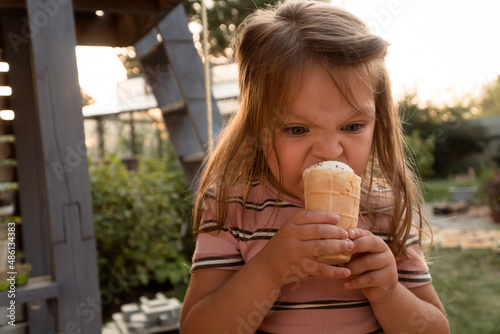 Little three years old girl holding ice cream in hands in backyard at summer