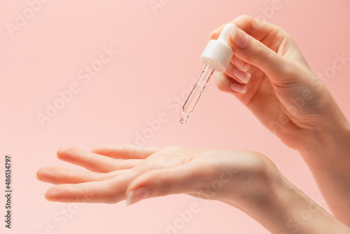 A woman drips serum from a pipette into the palm of her hand. Close-up of hands on a pink background. Copy space. The concept of beauty care products