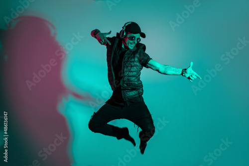 Fashionable handsome young man in stylish black clothes listens to music with headphones and dances on the jump in the studio