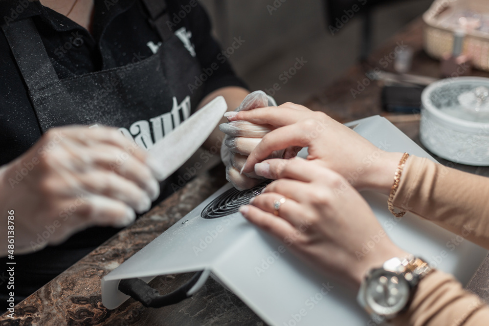 Obraz premium Female hands caring for nails, close-up. Woman does a manicure in a beauty salon. Professional saws a nail with a file