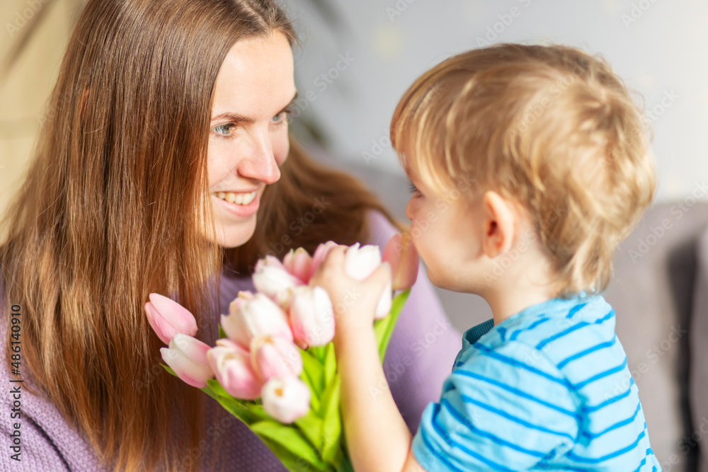 Beautiful blond boy, giving his mother a bouquet of tulips congratulating her on mother's day while celebrating the holiday at home Beautiful blond boy, giving his mother a bouquet of tulips congratulating her on mother's day while celebrating the holiday at home