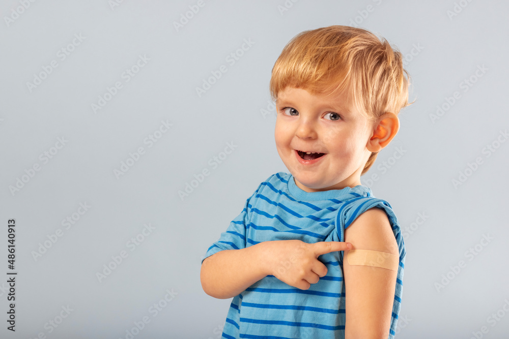 Vaccination of children. Happy vaccinated blonde kid boy showing arm with adhesive bandage after vaccine injection. Kids and covid-19 prevention, antiviral immunization - obrazy, fototapety, plakaty 