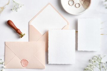 Wedding stationery set. Pastel pink wedding envelopes with wax seal stamp, wedding invitation card, golden rings on stone table. Flat lay, top view, copy space.