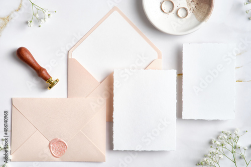 Wedding stationery set. Pastel pink wedding envelopes with wax seal stamp, wedding invitation card, golden rings on stone table. Flat lay, top view, copy space.