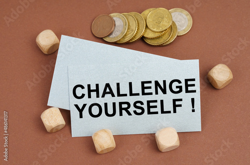On a brown surface are coins, cubes and a business card with the inscription - CHALLENGE YOURSELF