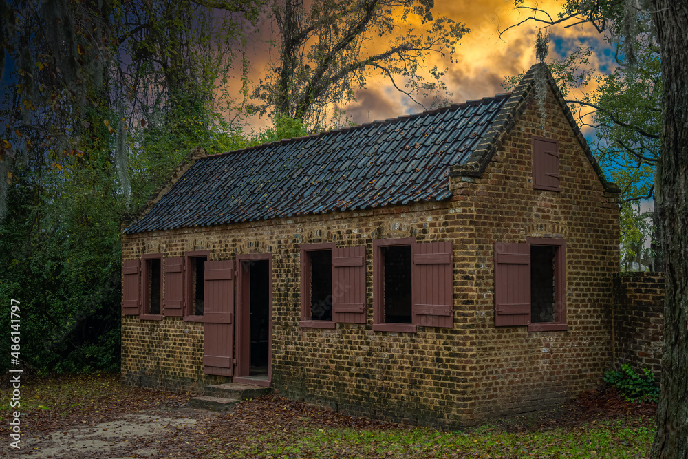 2022-02-09 A OLD ABANDONDED BRICK CABIN WITH WOOD TRIMMED WINDOWS SURROUNDED BY TREES WITH A ORANGE CLOUDY SKY