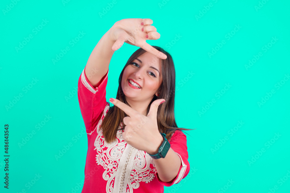 young beautiful moroccan woman wearing traditional caftan dress over green background making finger frame with hands. Creativity and photography concept.
