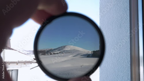 View of the snow-covered mountain peak through round tinted glass. The person holding camera 
ND filter and checking its opacity